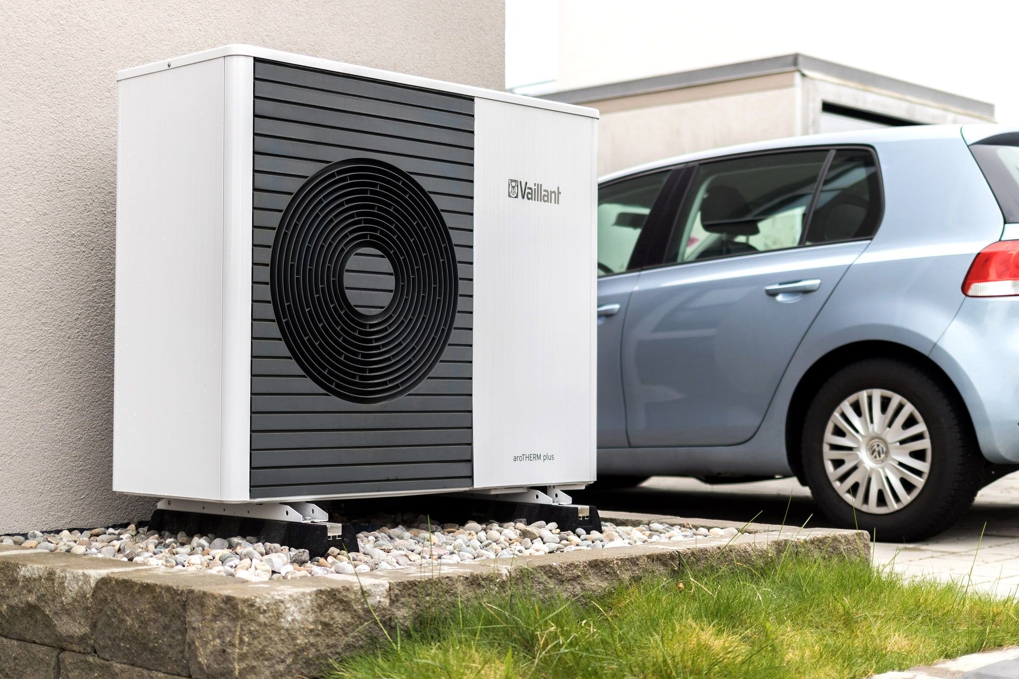 Moderne buitenunit van een warmtepomp naast een gestucte gevel