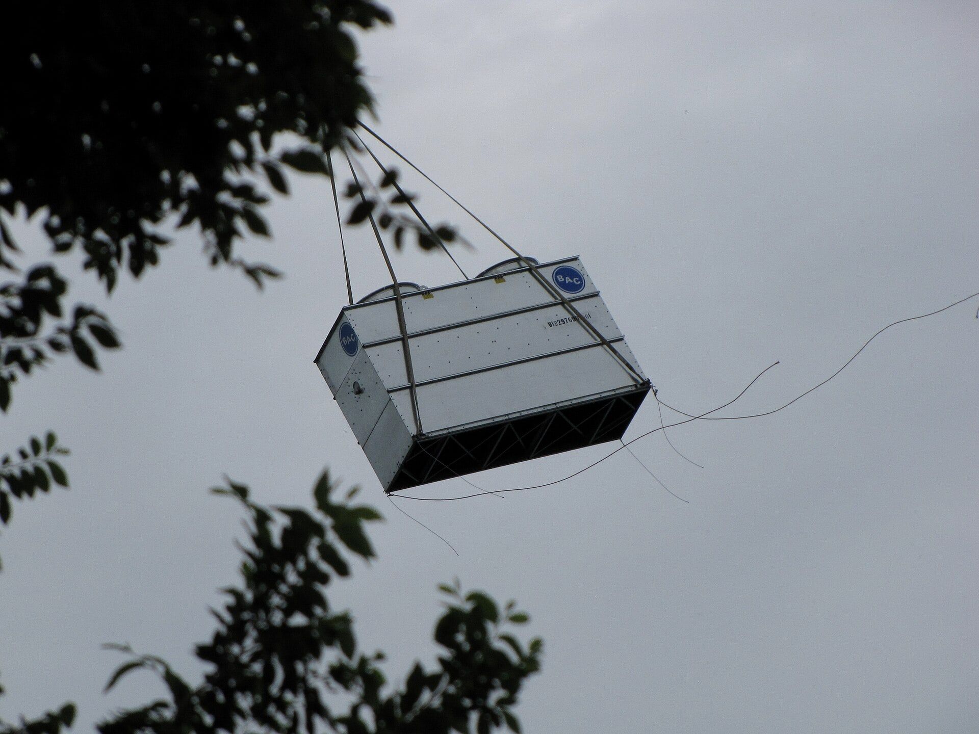 An air conditioning unit being lifted through the sky to a rooftop